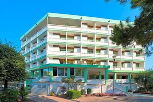 Un hotel a più piani con facciata verde e bianca, balconi e cielo sereno.