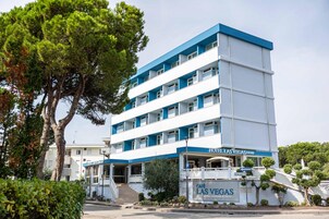Un hotel a più piani con facciata blu e bianca, un ingresso ben visibile e un cartello che indica 'Café Las Vegas', dove è possibile gustare bevande, cocktail e altro.