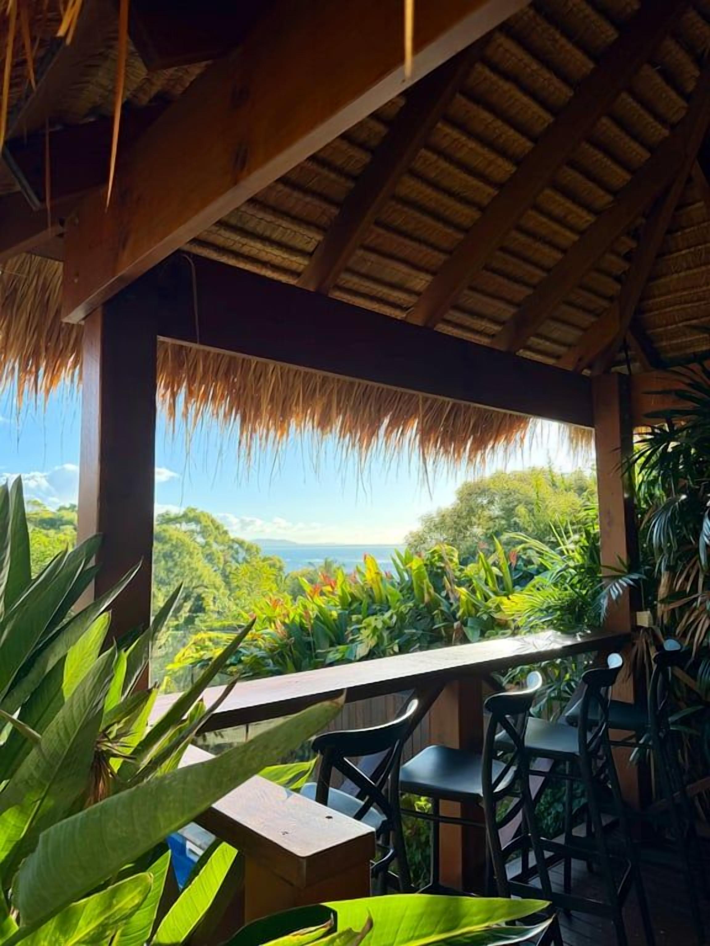 A covered outdoor seating area with a view of a lush landscape and the ocean.
