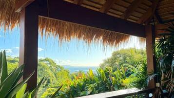A covered outdoor seating area with a view of a lush landscape and the ocean.