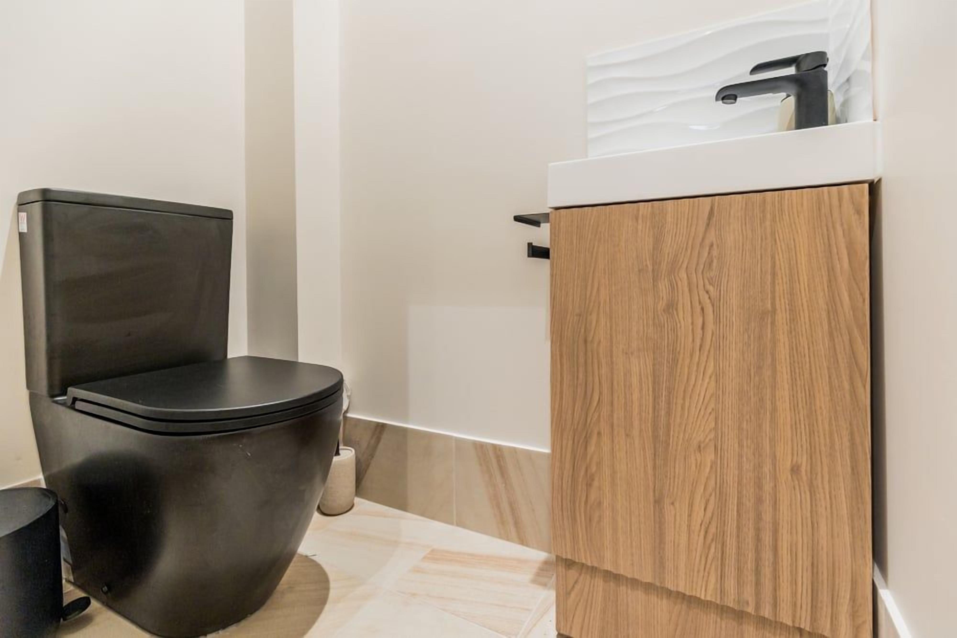 Un bagno moderno con un water nero, un mobiletto in legno e un ripiano bianco.
