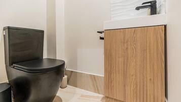 Un bagno moderno con un water nero, un mobiletto in legno e un ripiano bianco.