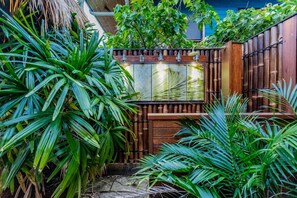 Un rigoglioso giardino con recinto in bambù, diverse piante verdi e un elemento d'acqua.
