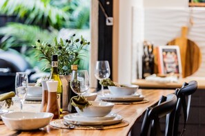A dining table set with white plates, bowls, and glasses, with a bottle of olive oil and a small plant on the table.