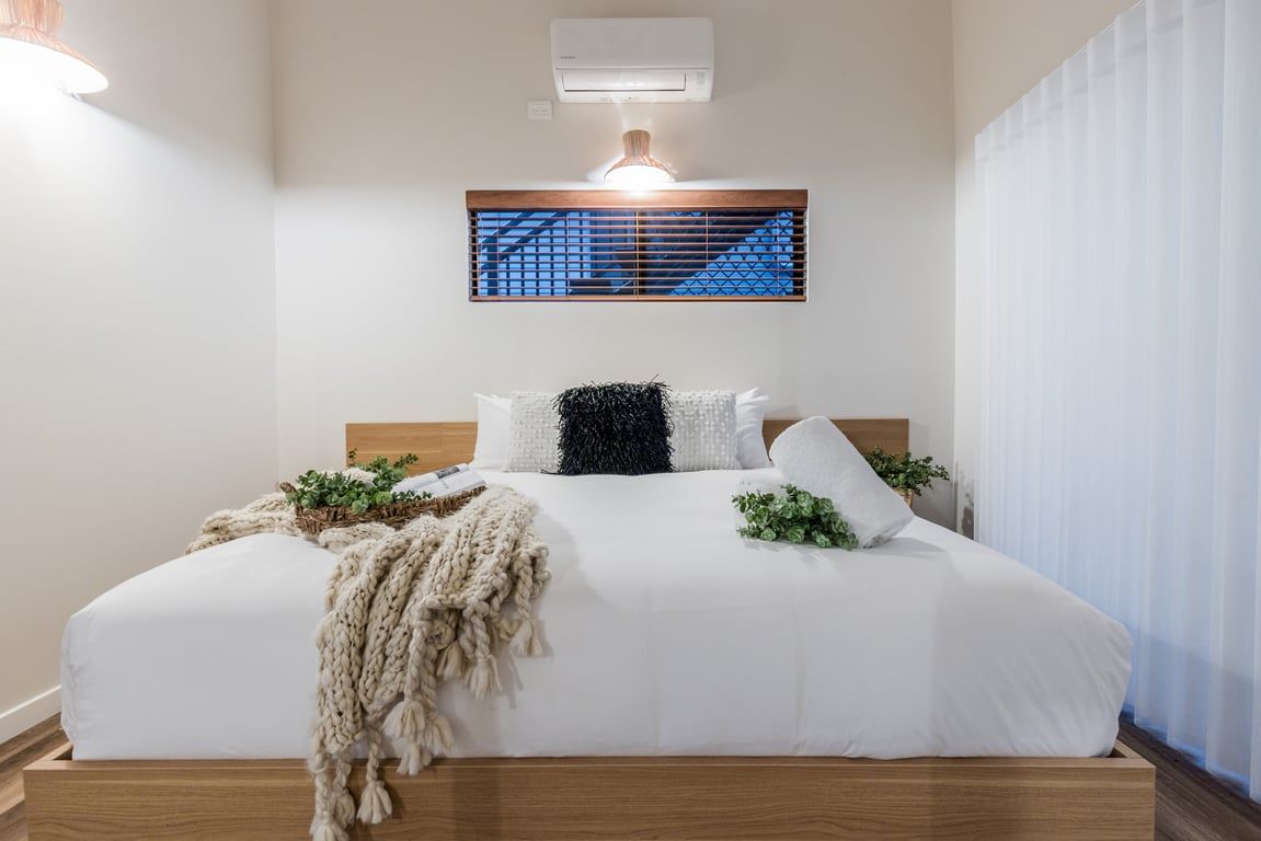 Ein Hotelzimmer mit Bett, Wandklimaanlage, Fenster mit Jalousien und einer Nachttischlampe.