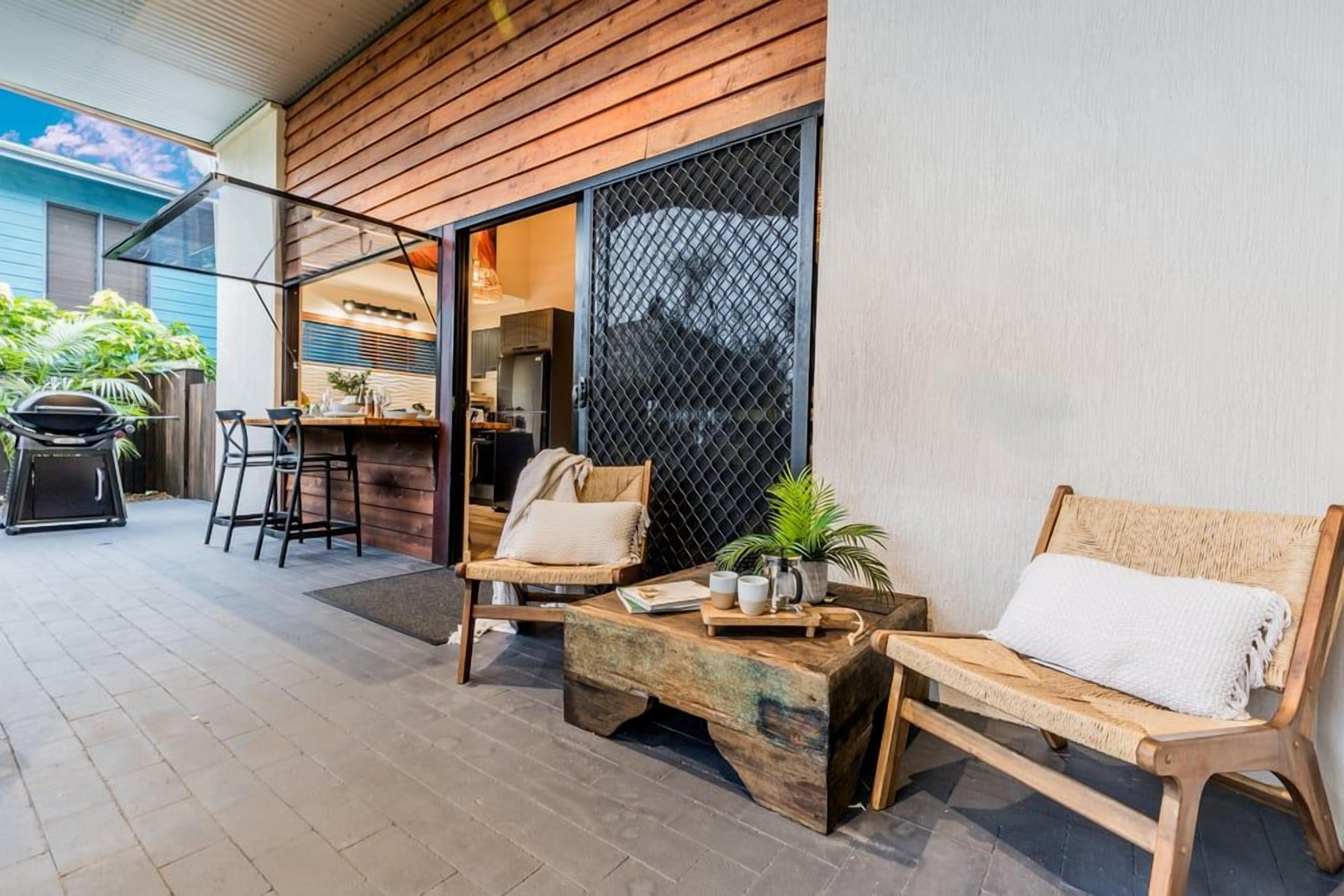 A patio area with a wooden bench, a table with a plant, and a grill.