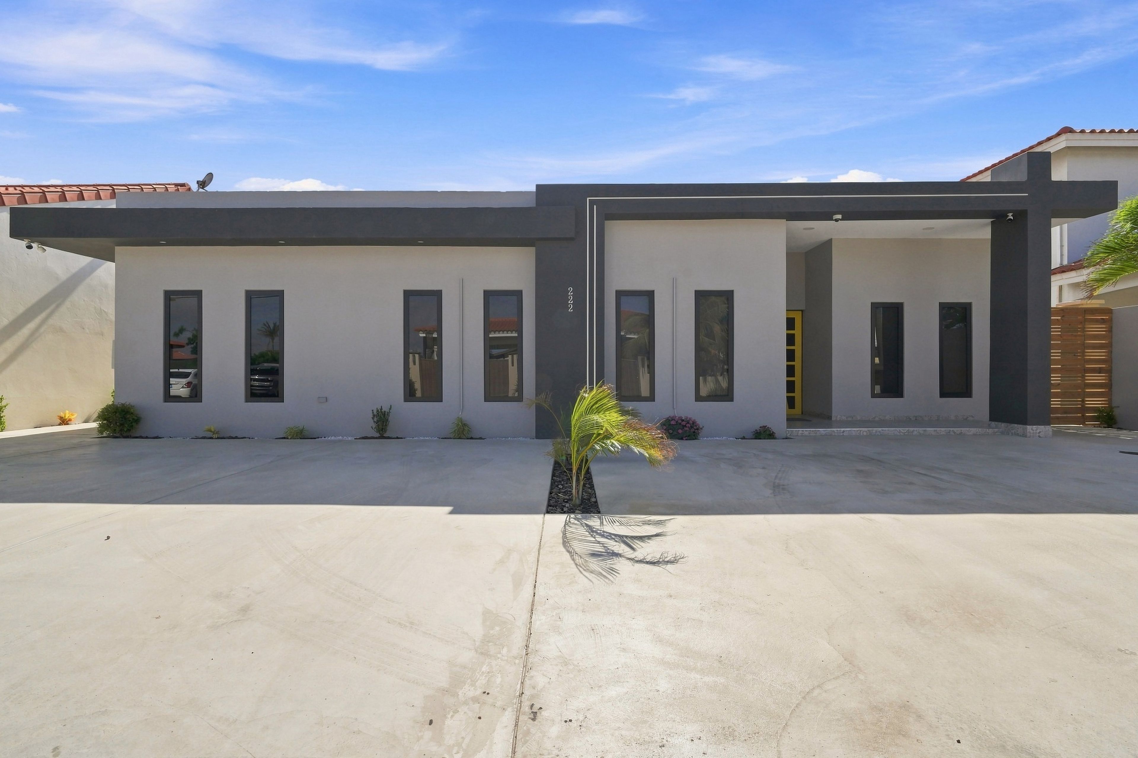 A modern two-story building with a flat roof, multiple windows, and a concrete driveway.