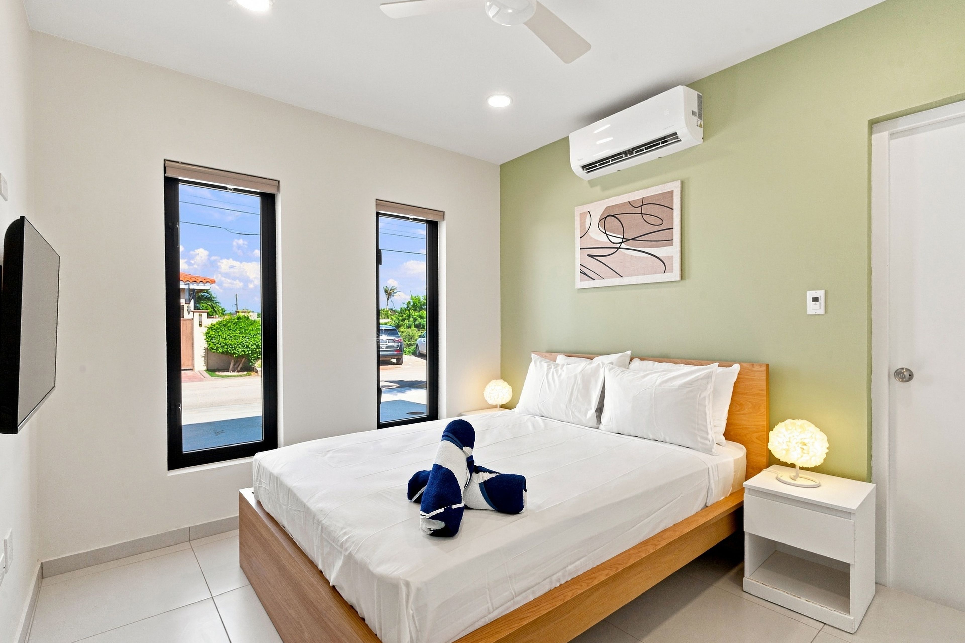 A hotel room with a bed, a nightstand, a wall-mounted air conditioner, and a window with a view of the street.