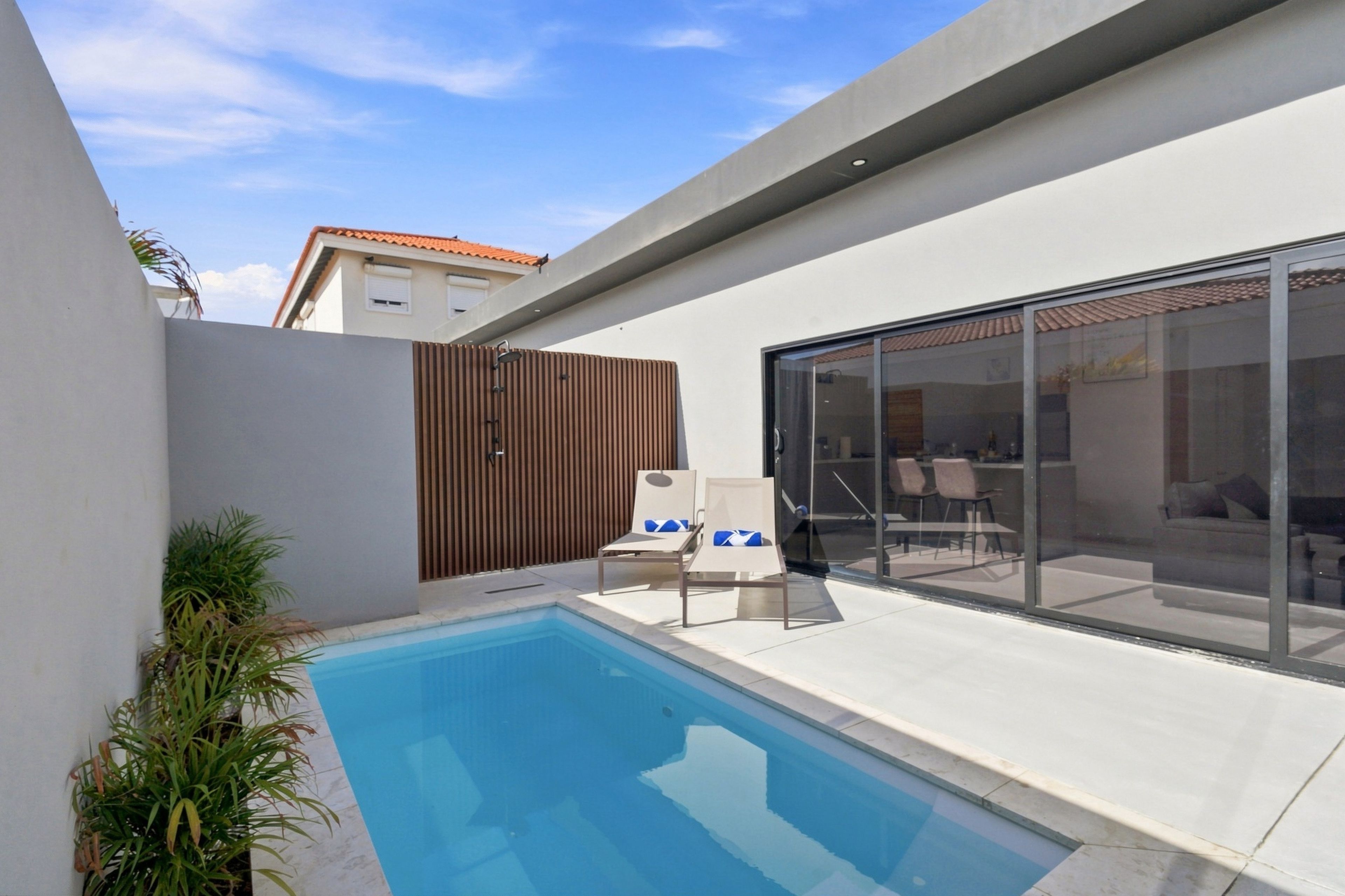 A modern outdoor pool area with a glass enclosure, lounge chairs, and a wooden fence.