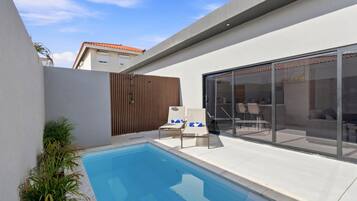 A modern outdoor pool area with a glass enclosure, lounge chairs, and a wooden fence.