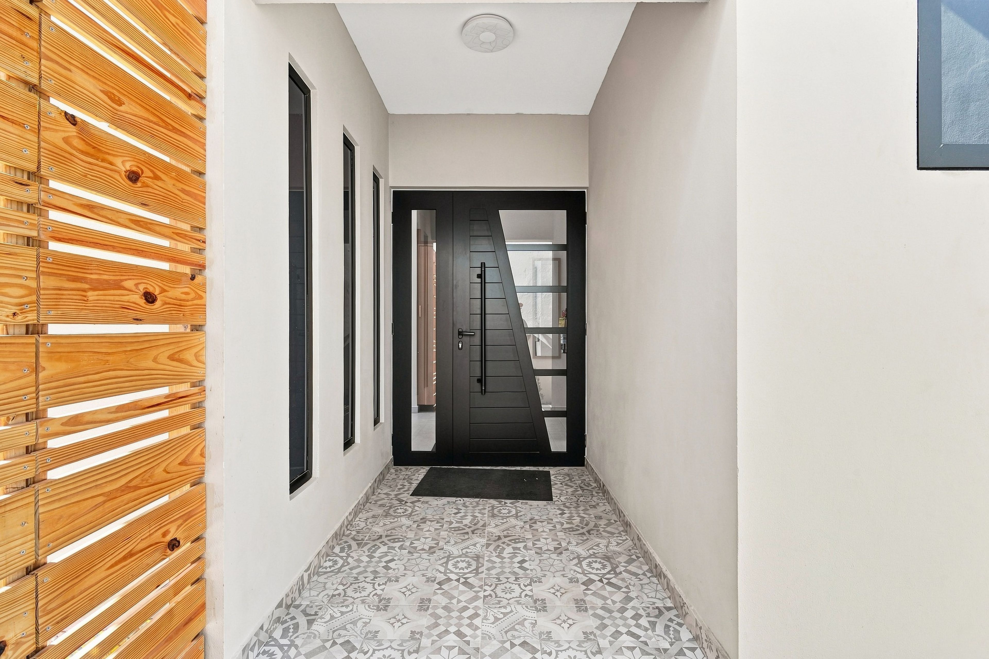 A hallway with a wooden slat wall, a black door with a window, and patterned floor tiles.