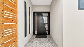 A hallway with a wooden slat wall, a black door with a window, and patterned floor tiles.