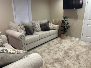 Een woonkamer met een beige bank, gestreepte kussens, een potplant en een wandgemonteerde flatscreen televisie.