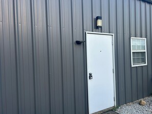 A metal building with a white door, a small window, and a wall-mounted light fixture.