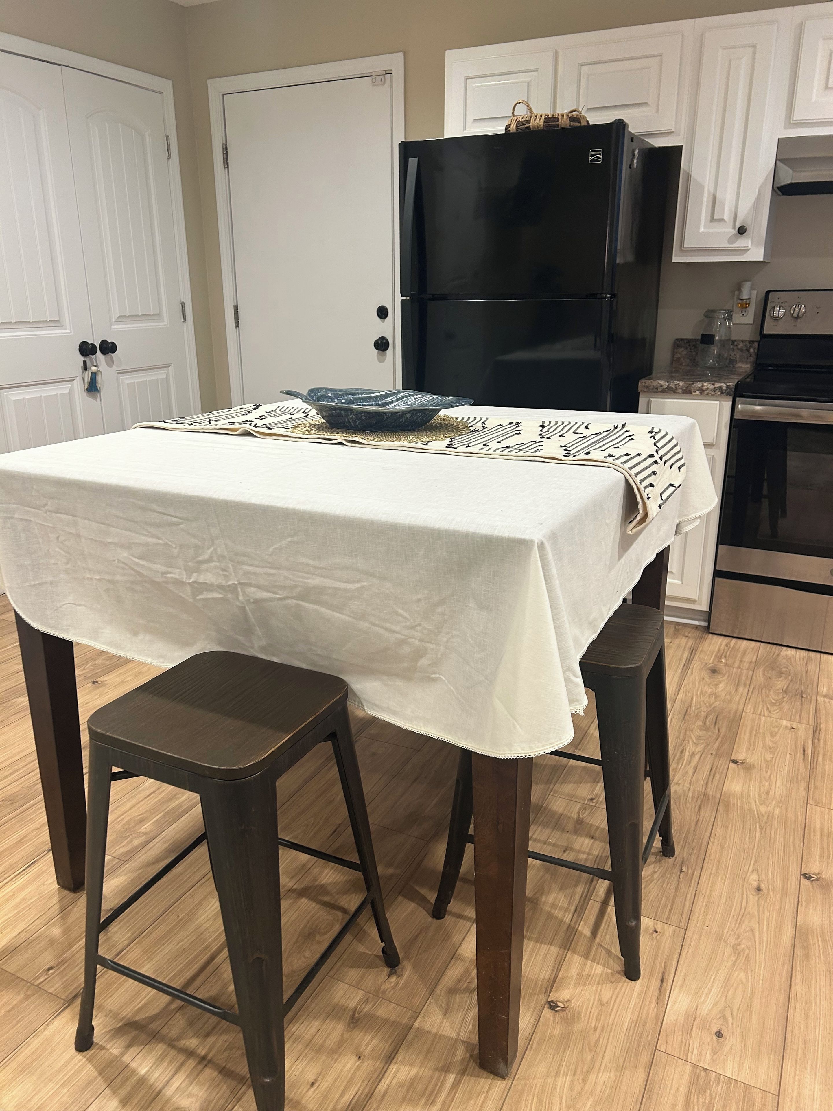 Una cocina con una mesa para dos, un refrigerador negro y piso de madera.