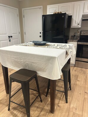 Een keuken met een tafel voor twee personen, een zwarte koelkast en houten vloeren.
