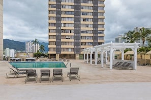 A hotel pool area with a large pool, lounge chairs, and a white pergola. - Waikiki Studio | Pool + Beach Gear | City Views (Honolulu)