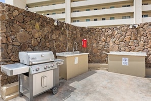 An outdoor barbecue area with a stone wall, a grill, and a trash bin. - Waikiki Studio | Pool + Beach Gear | City Views (Honolulu)