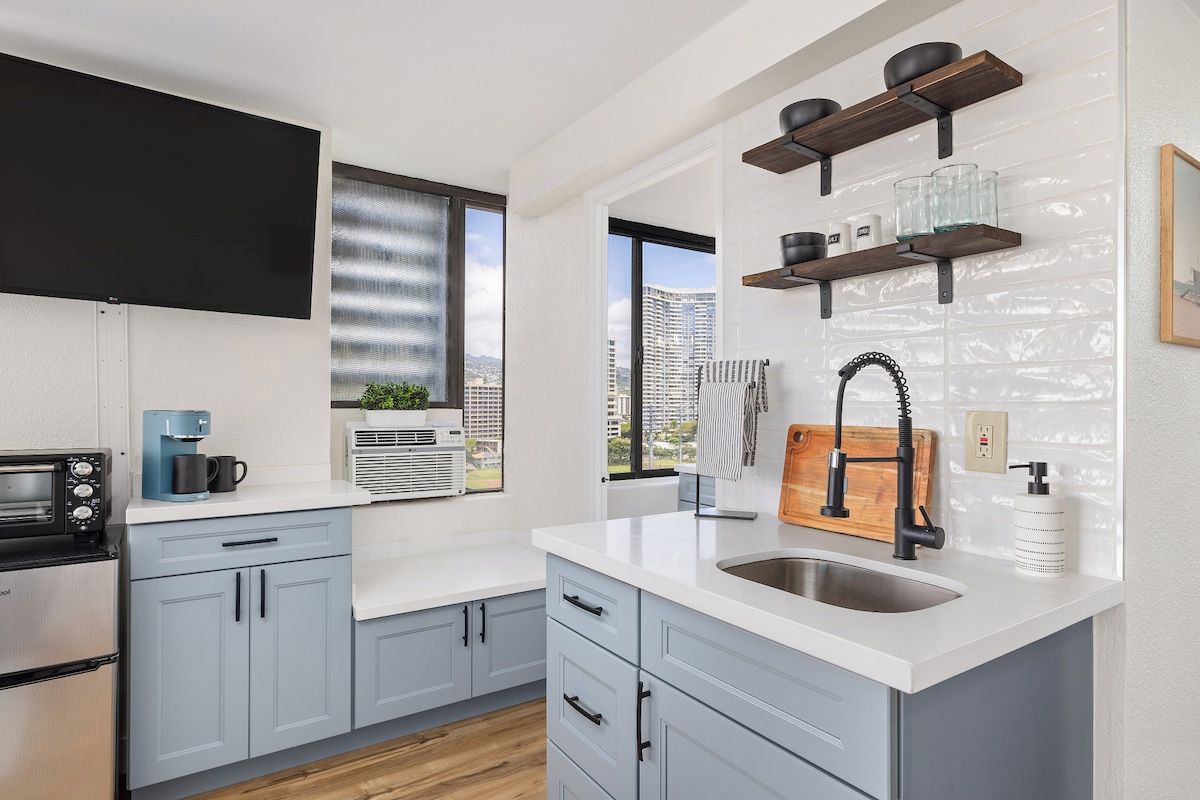 A modern kitchen with a built-in oven, a coffee maker, and a window with a view of buildings.