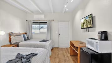A hotel room with two beds, a desk, a microwave, and a TV.