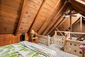 Ein Schlafzimmer im Dachgeschoss mit Holzboden, einem Bett, einem Nachttisch, einer Lampe und einem Deckenventilator.