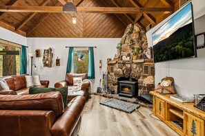 Ein gemütliches Wohnzimmer mit Kamin aus Stein, Ledermöbeln und einem an der Wand befestigten Fernseher.