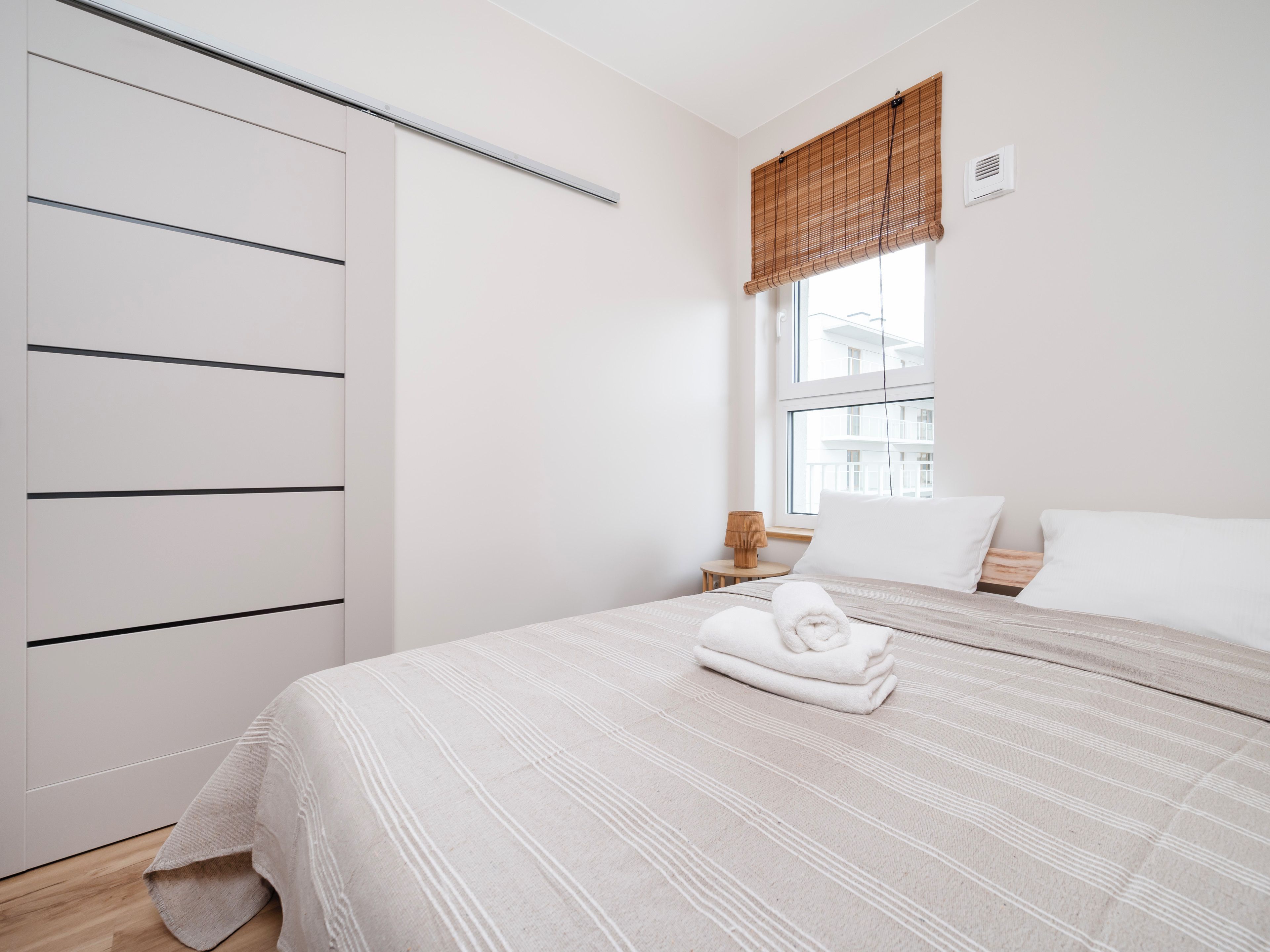 Ein Schlafzimmer mit Bett, Fenster mit Aussicht, Kleiderschrank und Nachttisch mit Lampe.