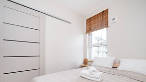 Ein Schlafzimmer mit Bett, Fenster mit Aussicht, Kleiderschrank und Nachttisch mit Lampe.