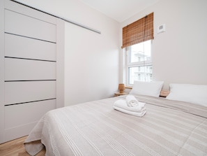 Ein Schlafzimmer mit Bett, Fenster mit Aussicht, Kleiderschrank und Nachttisch mit Lampe.