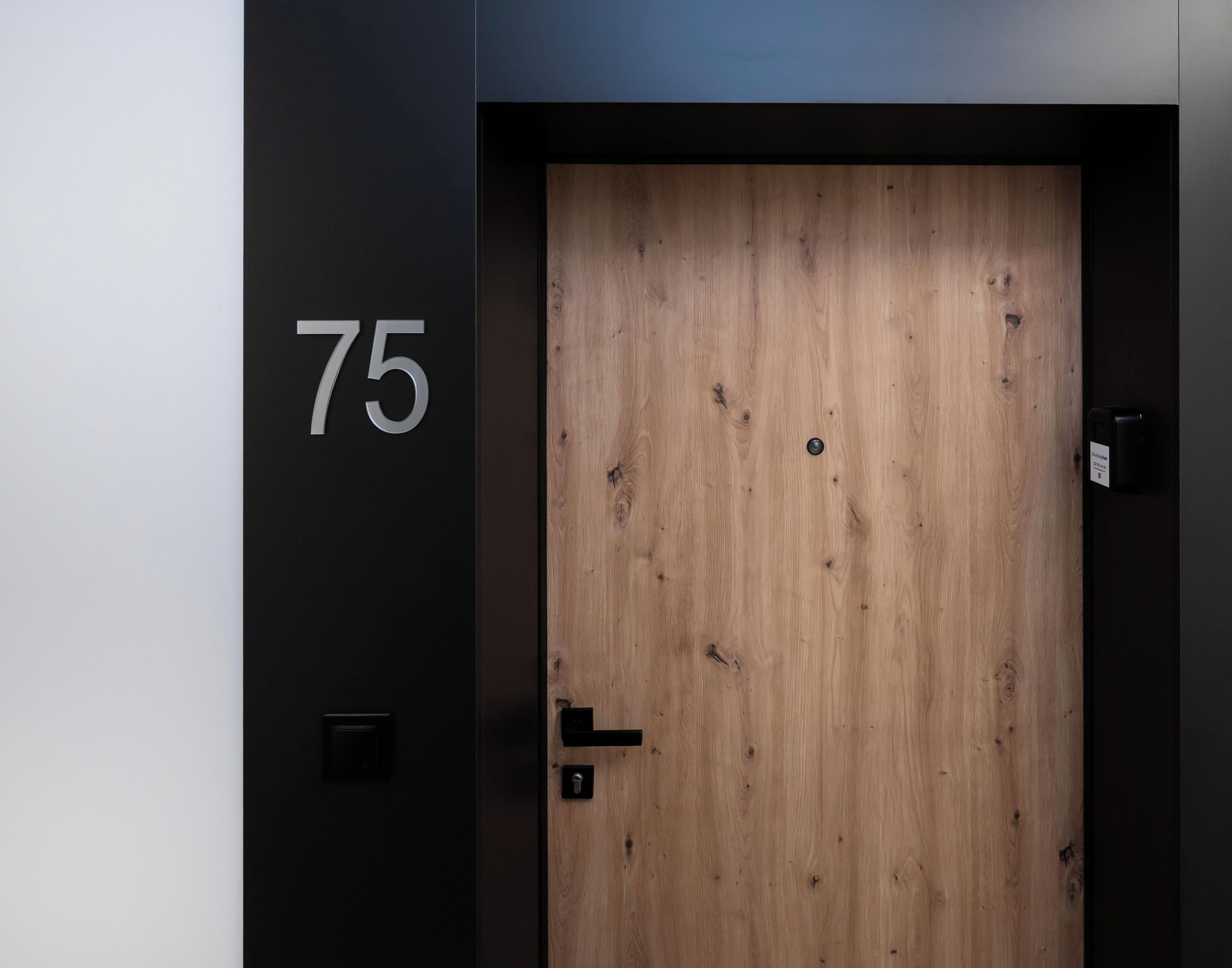 A wooden door with a number '75' on the wall to its left.