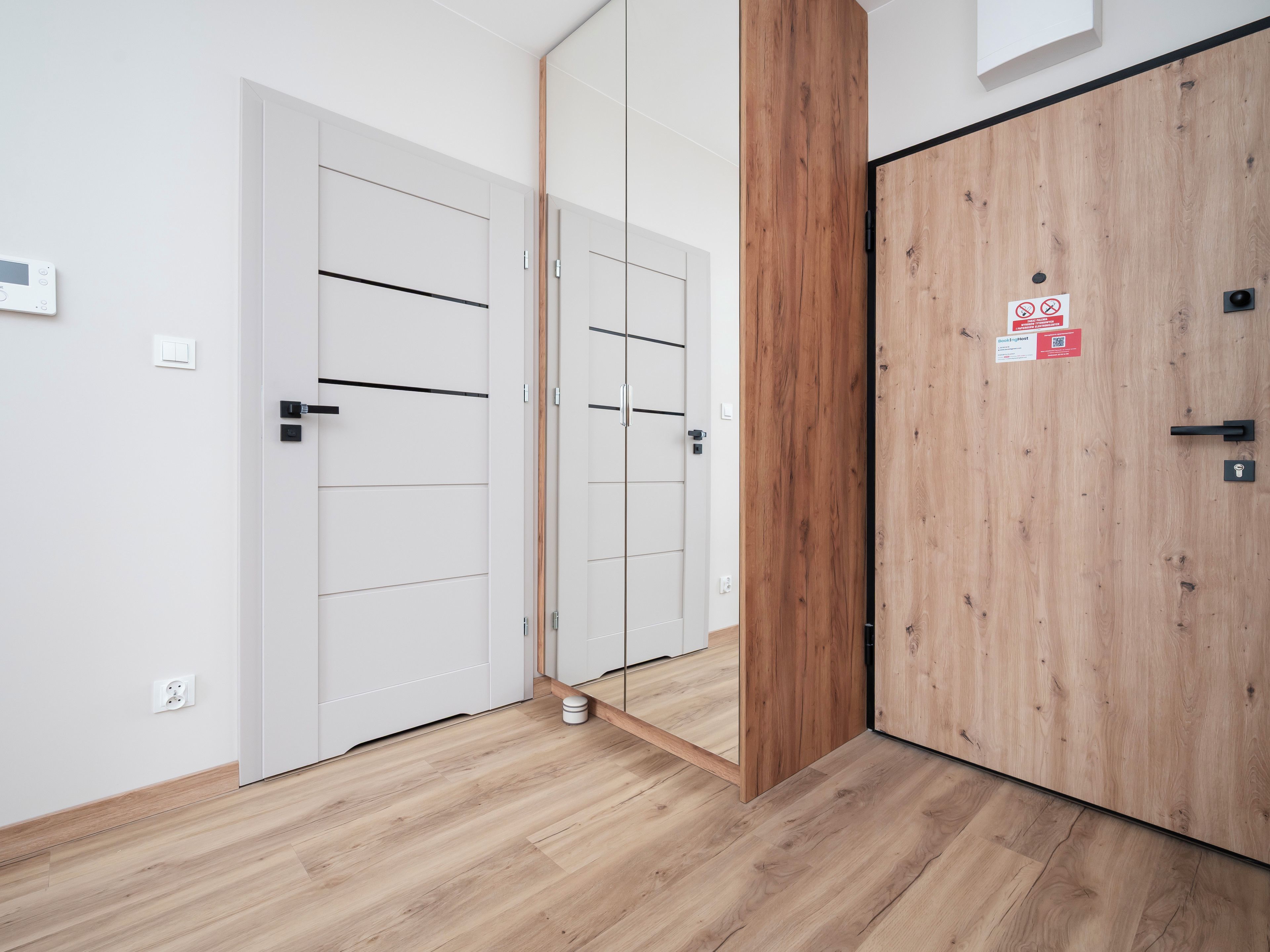 Corredor com portas brancas, uma porta de madeira e piso com acabamento em madeira clara.