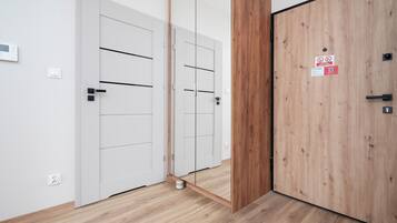 Corredor com portas brancas, uma porta de madeira e piso com acabamento em madeira clara.