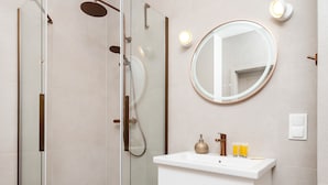 Ein modernes Badezimmer mit einer einteiligen Duschkabine, einem weißen Waschtisch mit rundem Spiegel und einer Wandleuchte.