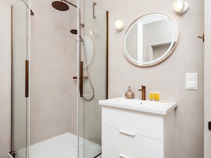 Ein modernes Badezimmer mit einer einteiligen Duschkabine, einem weißen Waschtisch mit rundem Spiegel und einer Wandleuchte.