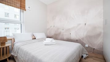 Ein Hotelzimmer mit einem großen Bett, einem Holznachttisch, einem Fenster mit Jalousien und einer Wand mit strukturierter Oberfläche.