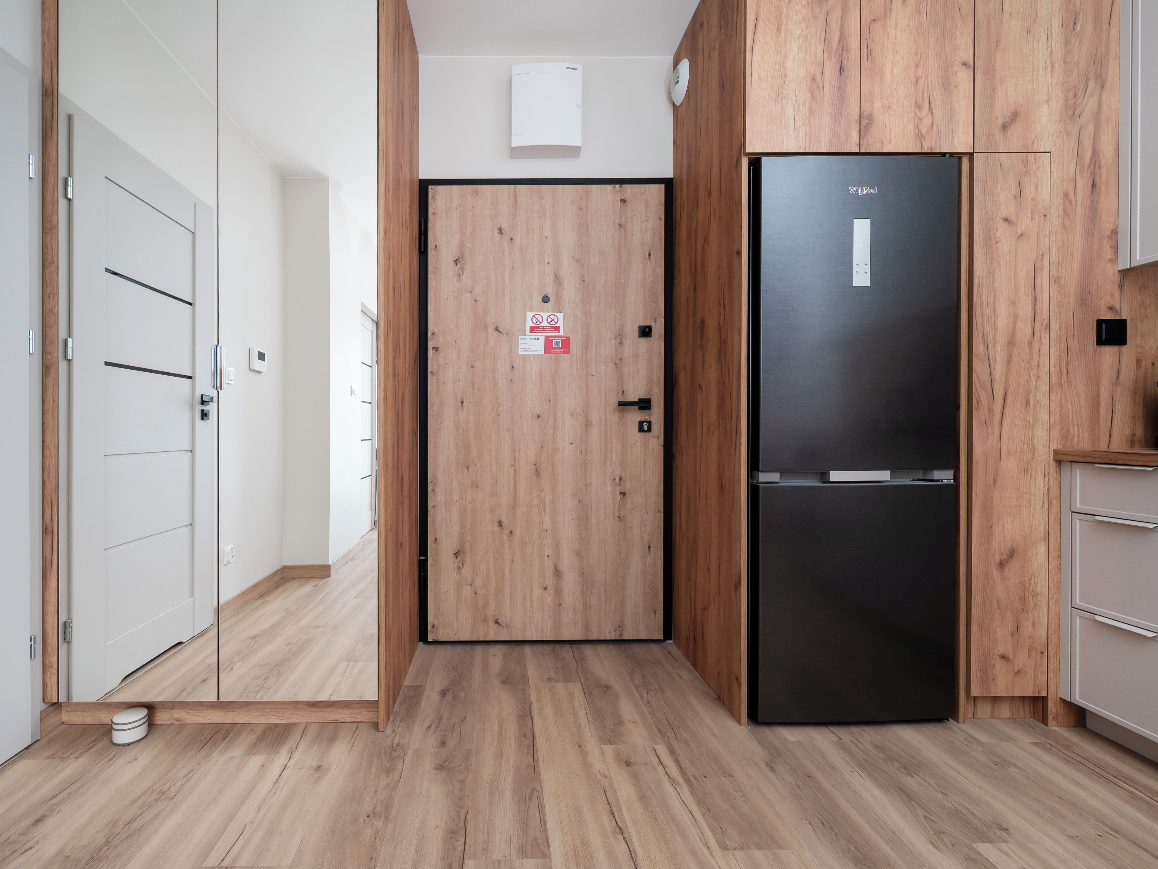 Une cuisine moderne avec des meubles en bois, un réfrigérateur noir et une porte ornée d’un panneau de signalisation de sécurité.