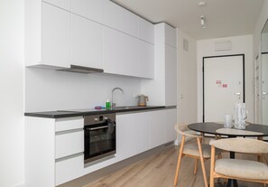 A modern kitchen with white cabinetry, a built-in oven, and a black countertop. There is a dining area with a round table and two chairs. - Browary Warszawskie Boutique Studio (Warszawa)