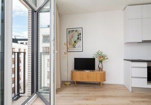 A modern apartment with a large sliding glass door, a wooden cabinet with a flat-screen TV, and a framed botanical artwork on the wall. - Browary Warszawskie Boutique Studio (Warszawa)