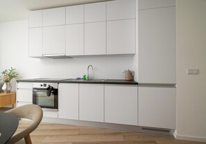 A modern kitchen with white cabinets, a stainless steel range hood, a built-in oven, and a black countertop. - Browary Warszawskie Boutique Studio (Warszawa)