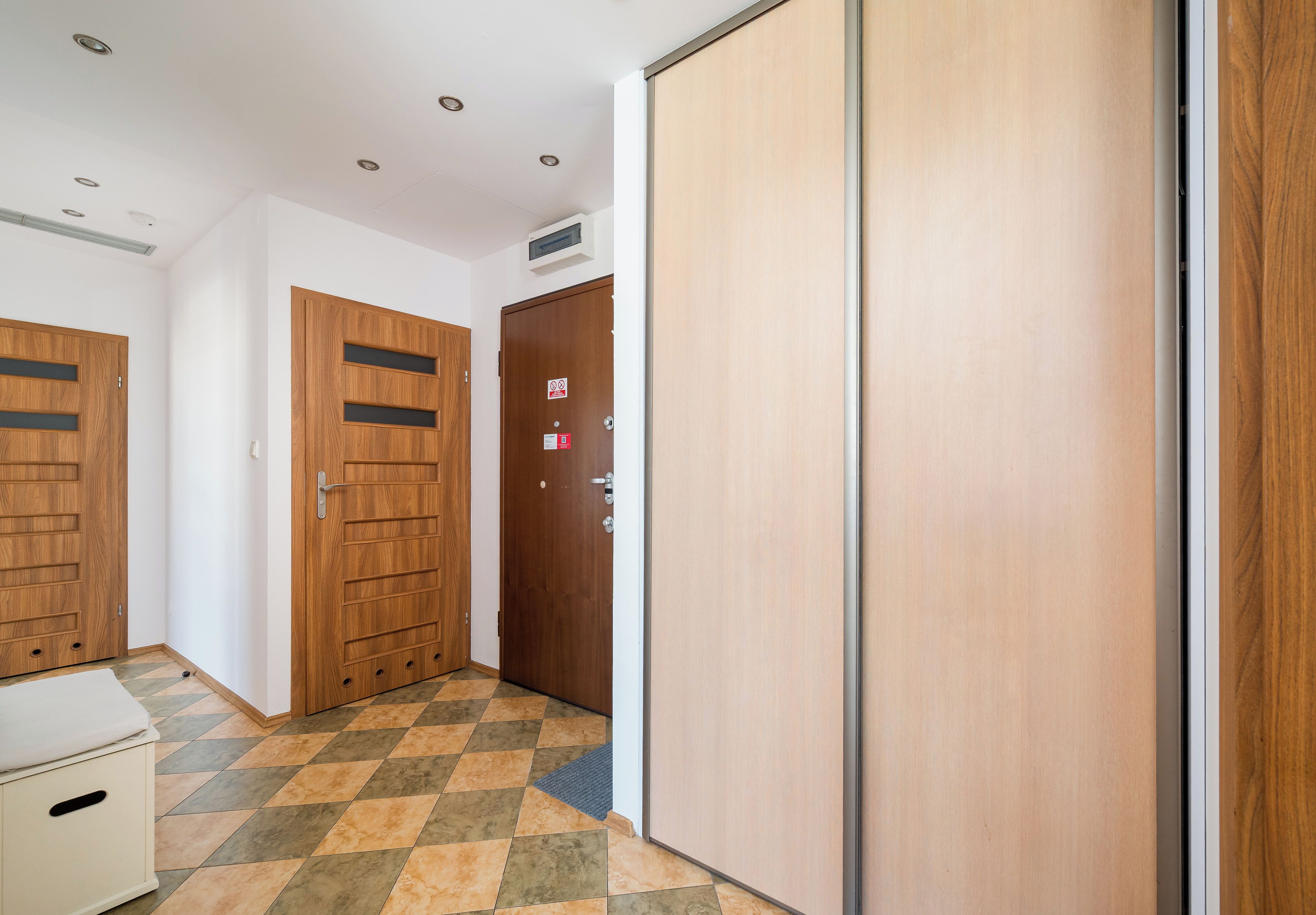 Un couloir avec deux portes en bois, un mur blanc, un sol carrelé et un petit meuble blanc.