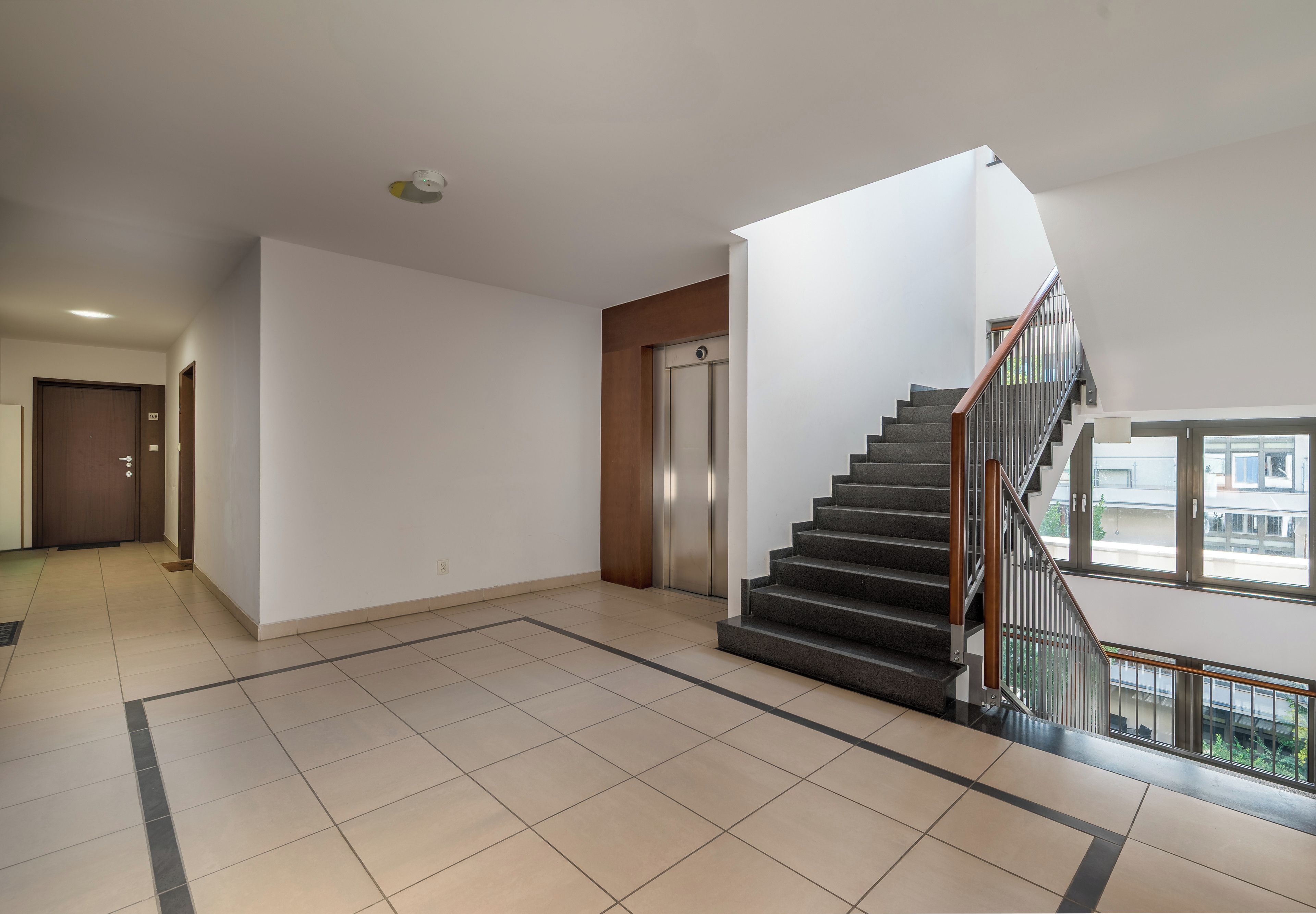 Un intérieur spacieux et moderne, avec un escalier, un ascenseur et une vue par une fenêtre.