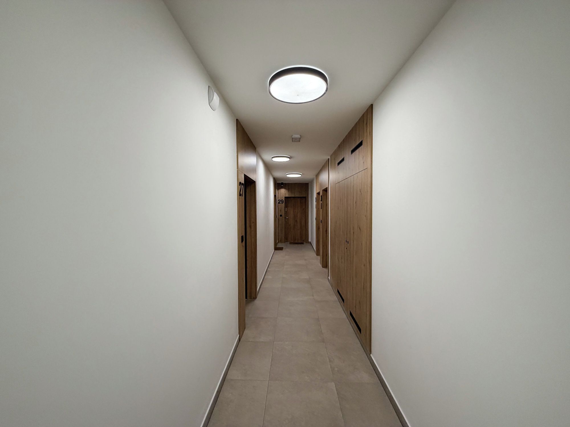 A hallway with lockers on both sides, a tiled floor, and recessed lighting.