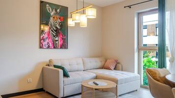 A living room with a sofa, a round coffee table, a painting, and a window with curtains.
