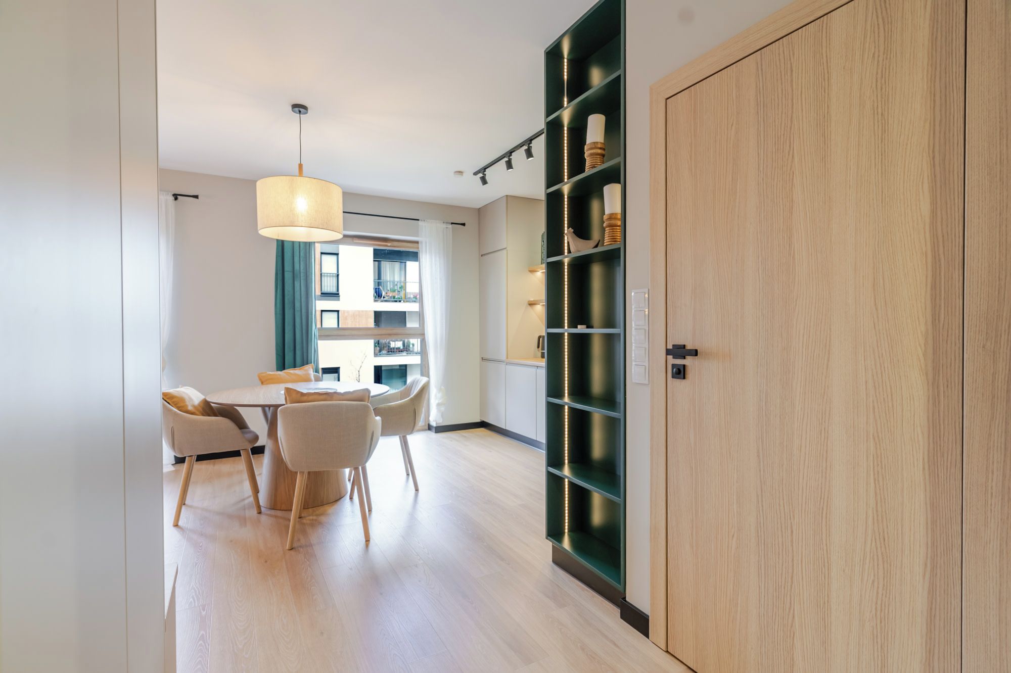 A modern interior with a dining area, a wooden wardrobe, and a green shelving unit with lights.
