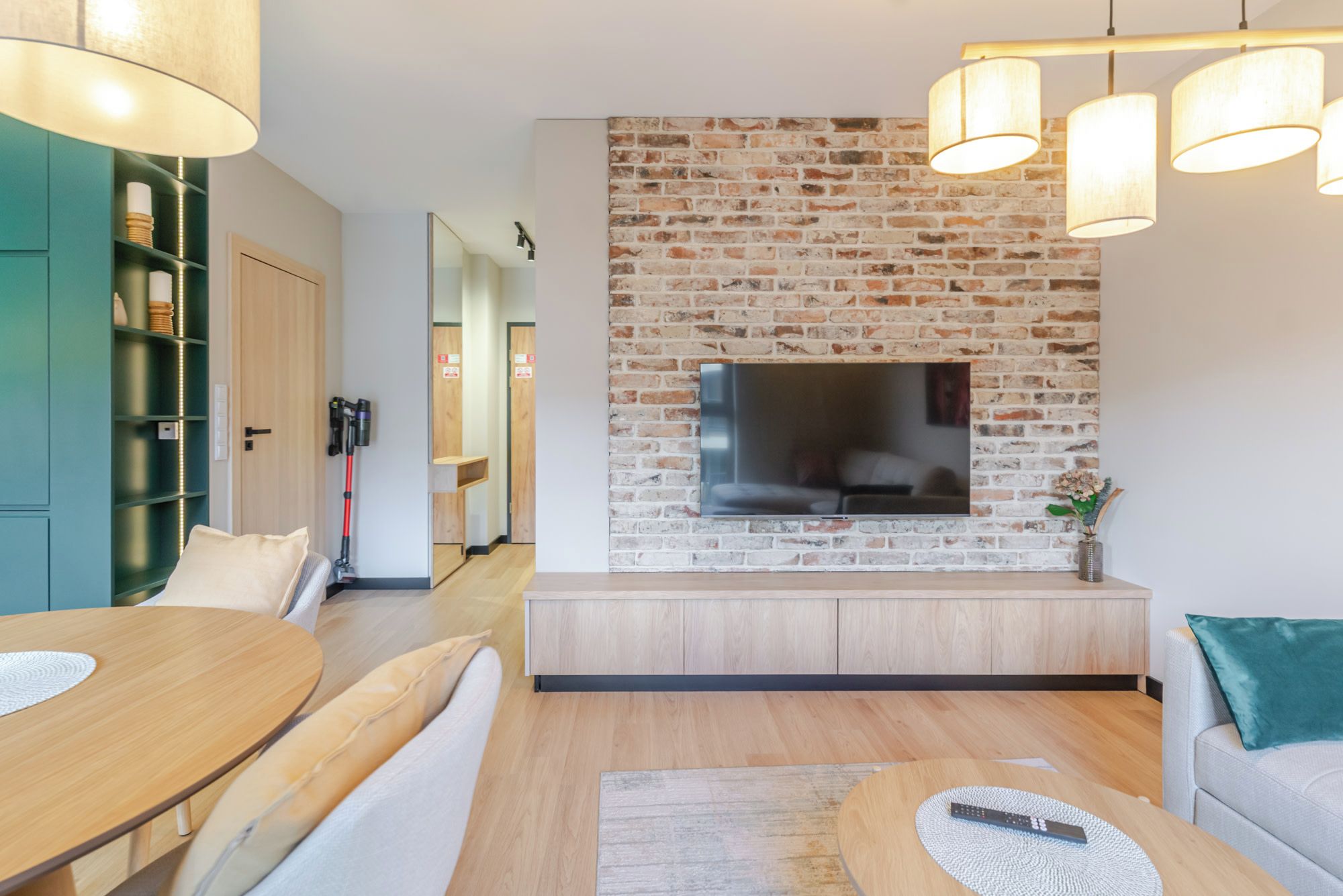 A modern living room with a brick wall, a flat-screen TV, a wooden coffee table, and a sofa.