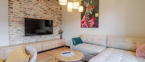 A living room with a brick wall, a flat-screen TV, a sofa, a coffee table, and a painting.