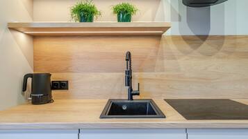 A modern kitchen with a built-in sink, a kettle, and a small potted plant on the countertop.