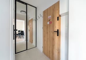 A hallway with a sliding glass door leading to a room, a wooden door with a sign, and a door handle. - Mokotów Rzymowskiego Urban Apartment (Warszawa)