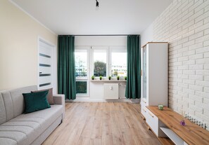 A modern living room with a sofa, a wooden floor, a white brick wall, and a window with curtains. - Mokotów Rzymowskiego Urban Apartment (Warszawa)