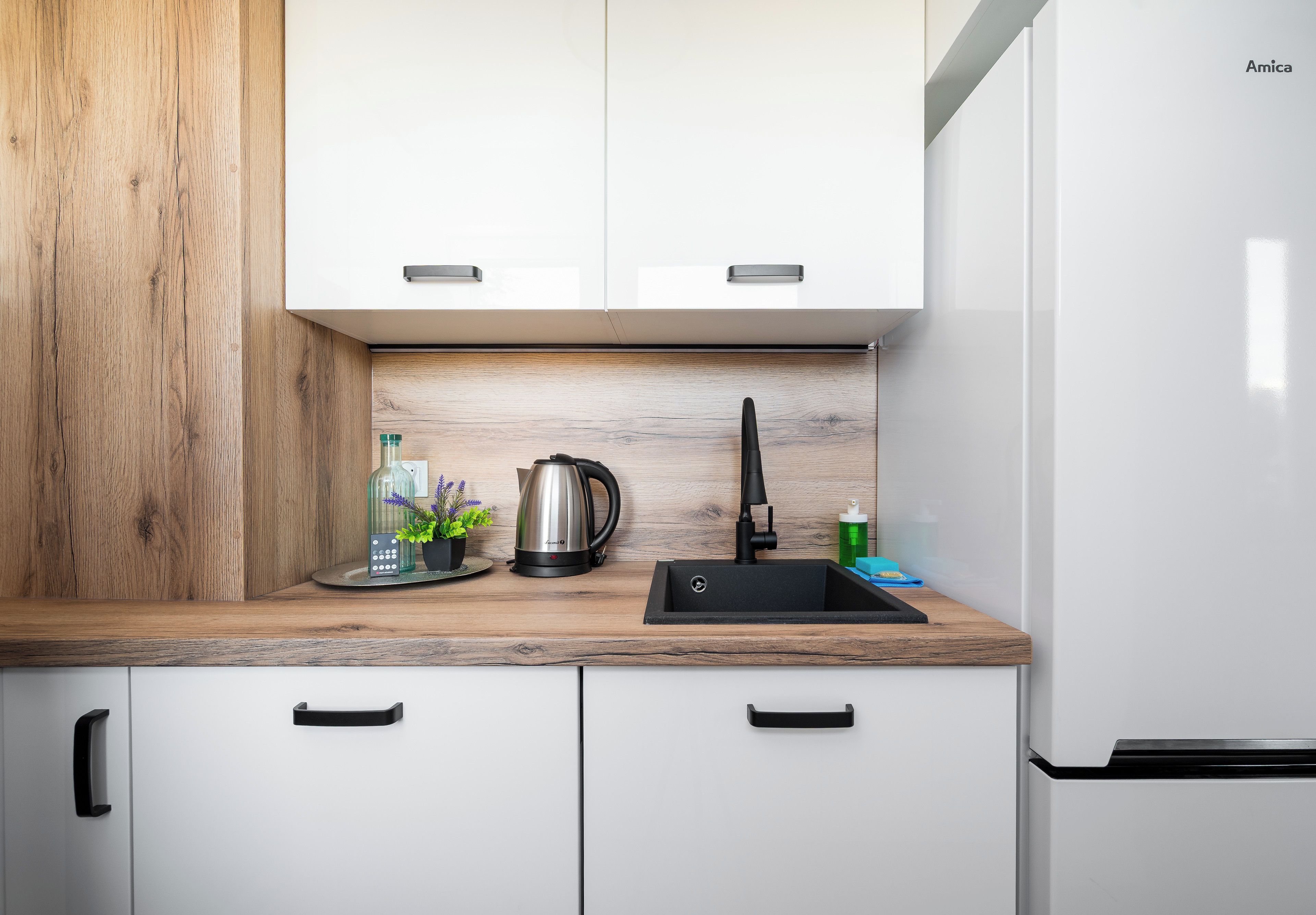 Een moderne keuken met witte kasten, een houten accentmuur, een zwart spoelgedeelte en een roestvrijstalen waterkoker.